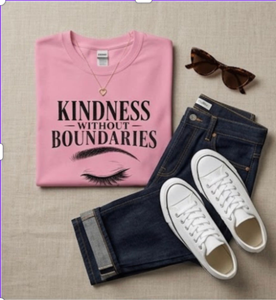 Pink t-shirt with 'Kindness without Boundaries' text, sunglasses, jeans, and white sneakers on a beige surface.